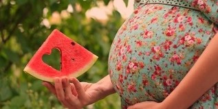 Fatia de melancia na mão de uma mulher grávida